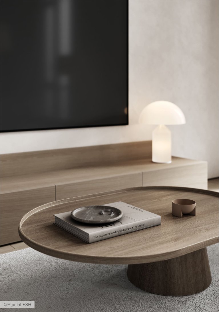 В гостиной на круглом деревянном журнальном столике лежат книги, декоративная тарелка и подсвечник. На заднем плане виден телевизор и современный светильник.