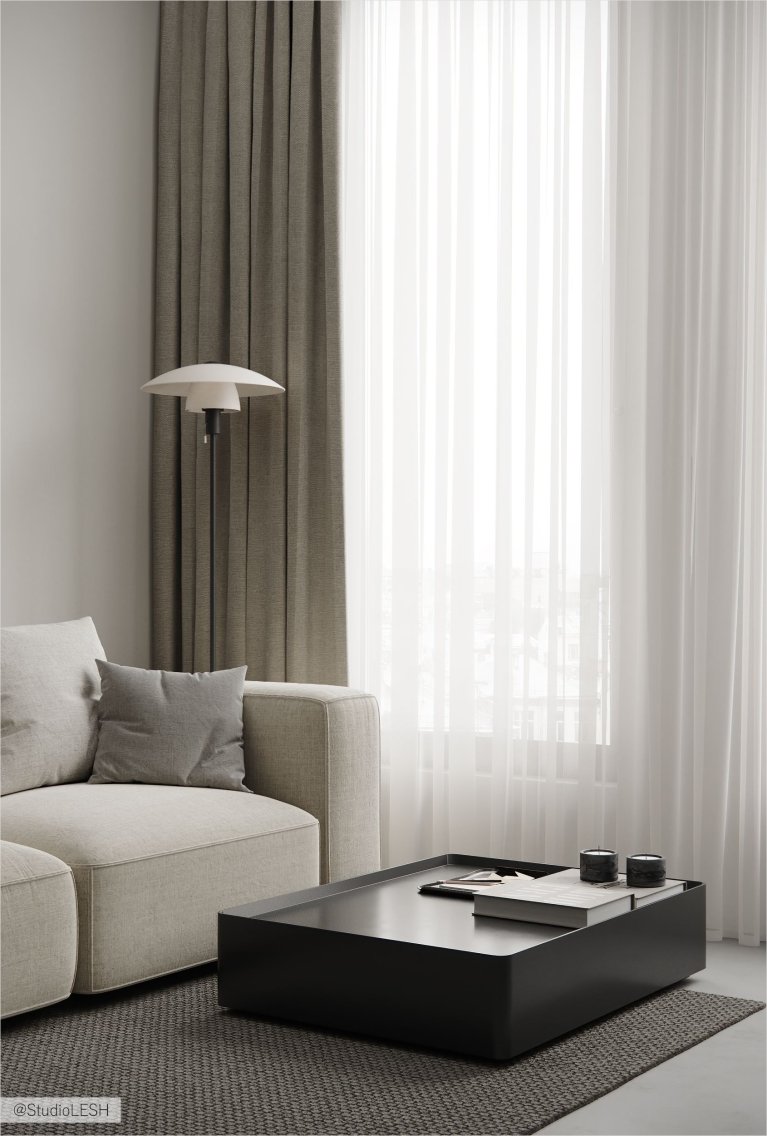 Интерьер современной гостиной с белым диваном, серым креслом, черным журнальным столиком и большими окнами с плотными шторами.