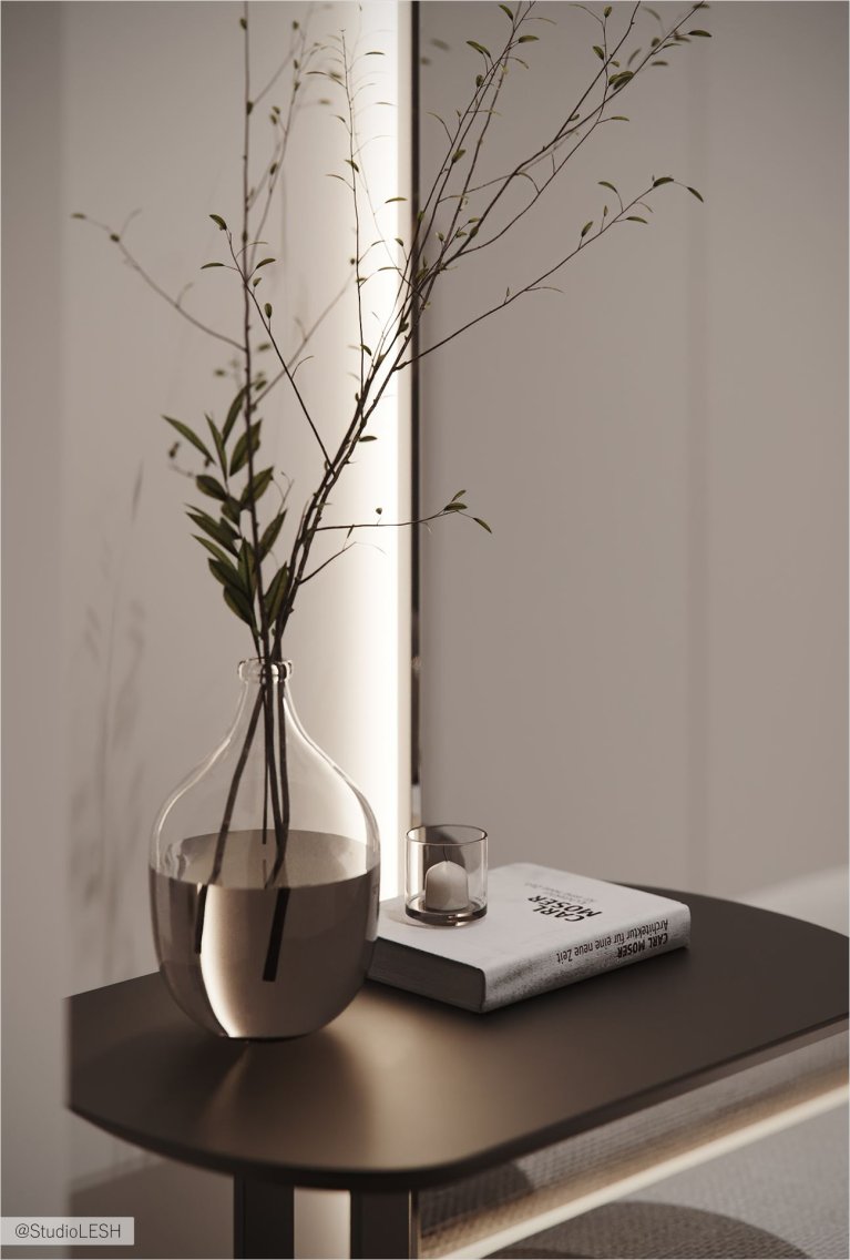 На фотографии изображен минималистичный интерьер с комнатными растениями в прозрачной вазе на столе. Рядом с вазой лежит открытая книга и декоративный подсвечник. Стена за столом светлая, с точечным освещением