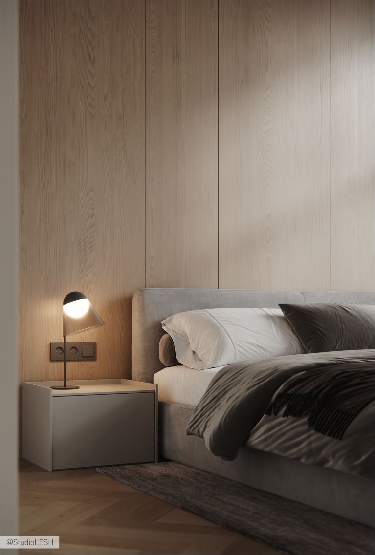 Уютная спальня с большой кроватью, застеленной серым покрывалом, и декоративными подушками. На стене за кроватью - деревянная панель, а по бокам - две тумбочки с лампами. В комнате также есть большое окно с жалюзи и плотными шторами, пропускающими мягкий свет