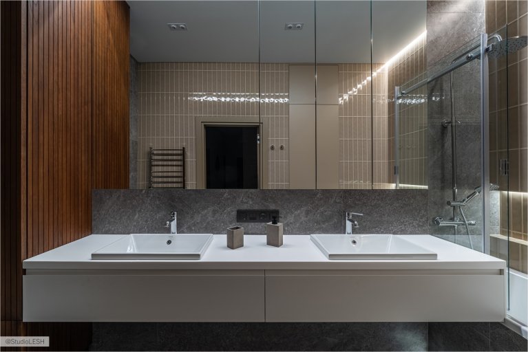 Под зеркалом находится раковина с белым цветом, на которой стоят мыло и другие банные принадлежности